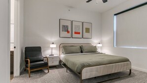 A bedroom with a bed, a chair, a nightstand, a ceiling fan, and wall art. - New LUX 2Bed Apt @ UCO (Edmond)