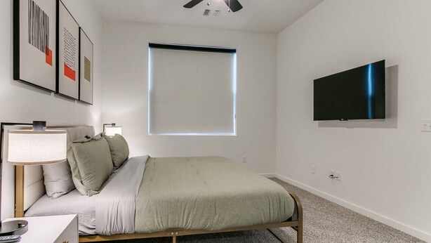 Ein Schlafzimmer mit einem Bett, einem Schreibtisch, einem Stuhl, einem Deckenventilator, einem Fenster und einem Fernseher.