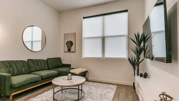 Ein modernes Wohnzimmer mit einem grünen Sofa, einem runden Couchtisch und einem großen Fenster.