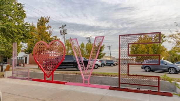 A street view with a large heart-shaped metal sculpture spelling 'LOVE' in the foreground. - New LUX 2Bed Apt @ UCO (Edmond)
