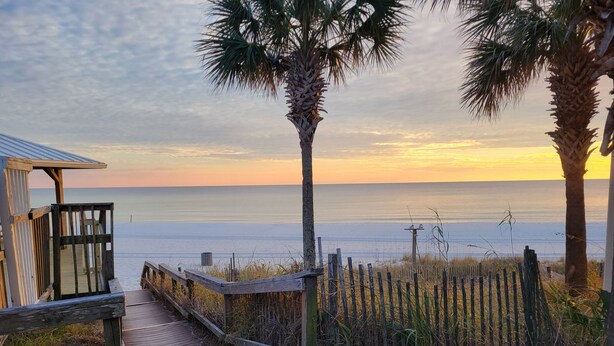 A wooden boardwalk leading to a beach with a wooden structure on the left.