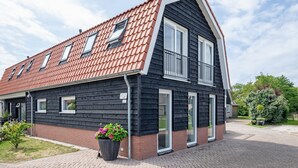 A two-story house with a red-tiled roof, black siding, and a brick foundation. - 2 Cosy Homes With Wellness Garden (Den Burg)