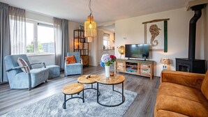 A modern living room with a sofa, armchairs, a coffee table, and a TV. - 2 Cosy Homes With Wellness Garden (Den Burg)