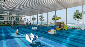 A children's play area with a view of the sea, featuring swings, slides, and a climbing structure.