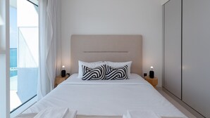 Quarto de hotel com cama, duas mesas de cabeceira com abajures, uma janela grande com cortinas e um guarda-roupa.
