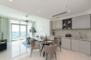 A modern living room with a dining area, a kitchen, and a large sliding glass door to the outside. - Stylish Emaar Beachfront 2BR w/ Beach Access (Dubai)