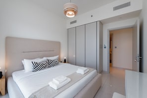 A modern hotel room with a neatly made bed, a wardrobe, and a bathroom visible through an open door.