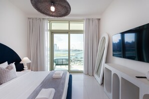 Une chambre d’hôtel moderne dotée d’un grand lit, d’une télévision à écran plat, d’une vue sur le paysage urbain et d’un balcon donnant sur le port de plaisance.