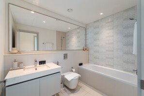 Une salle de bain moderne avec un grand miroir, une baignoire et des toilettes.