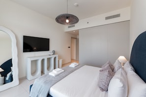 Una habitación de hotel moderna con una cama grande, un televisor de pantalla plana montado en la pared, una mesita de consola y un espejo amplio.