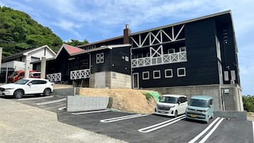 Un edificio moderno con fachada negra y detalles blancos, espacios de estacionamiento y un automóvil blanco estacionado al frente.