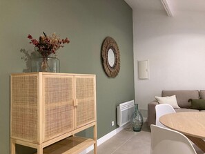 Un salon avec un meuble en rotin, un miroir rond, un canapé beige et une table ronde.