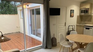 A modern room with a sliding glass door leading to a patio, a dining area with a table and chairs, a kitchen with a microwave and dishwasher, and a flat-screen TV mounted on the wall. - Cottage Saint-remy-de-provence (St.-Rémy-de-Provence)