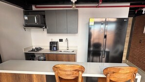 A modern kitchen with a central island, two wooden bar stools, a stainless steel refrigerator, and a built-in oven. - Duplex loft base  (Medellín)