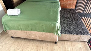 A bed with a green bedspread and a patterned mattress, a wooden door, and a brick wall. - Duplex loft base  (Medellín)