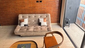 A modern living room with a brick wall, a beige sofa with cushions, a wooden coffee table, and a wooden chair. - Duplex loft base  (Medellín)