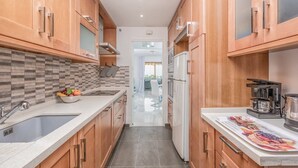 A narrow kitchen with wooden cabinets, a tiled backsplash, a sink, a bowl of fruit, and a coffee maker. - Cosy Apartment in Mijas (Mijas)