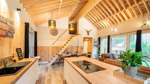 A modern kitchen with wooden accents, a central island, and a staircase leading to a loft area. - Escape With Heated Pool (Erezee)