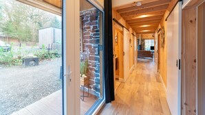 A modern interior with a wooden floor, stone wall, and sliding doors leading to a garden area. - Escape With Heated Pool (Erezee)