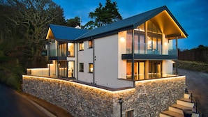Una casa moderna de dos pisos con base de piedra, ventanas grandes y exterior bien iluminado.