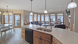 A spacious kitchen with a large island, wooden cabinets, and a dishwasher. There are pendant lights above the island and a flat-screen TV mounted on the wall.
