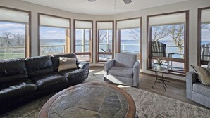 A spacious living room with a large stone coffee table, leather sofas, and a view of a lake through large windows.