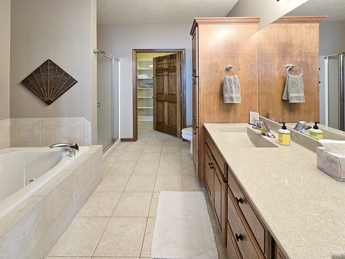 A modern bathroom with a large bathtub, a vanity with a sink, and a mirror. There is a towel rack with towels hanging on it, and a toilet visible in the background.