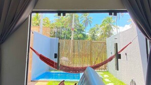 Ett rum med utsikt över en pool och palmer, en hängmatta och en säng med kuddar.