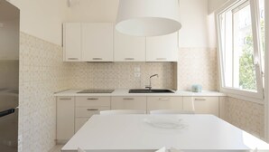 Una cocina moderna con armarios blancos, una isla grande con sillas, un ventanal con vistas y una lámpara colgante.