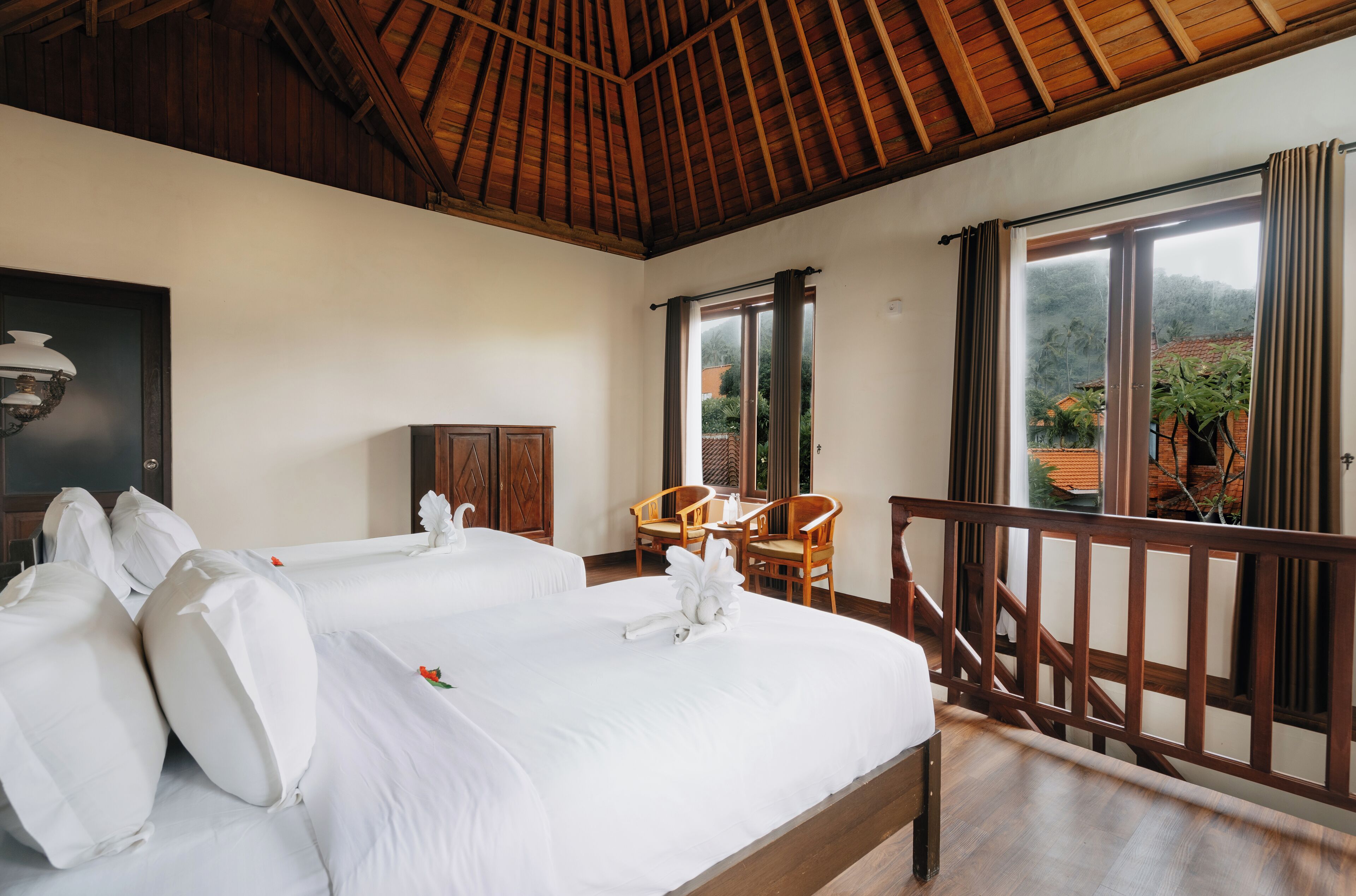 Habitación de hotel con dos camas, muebles de madera y un balcón con vistas al paisaje circundante.