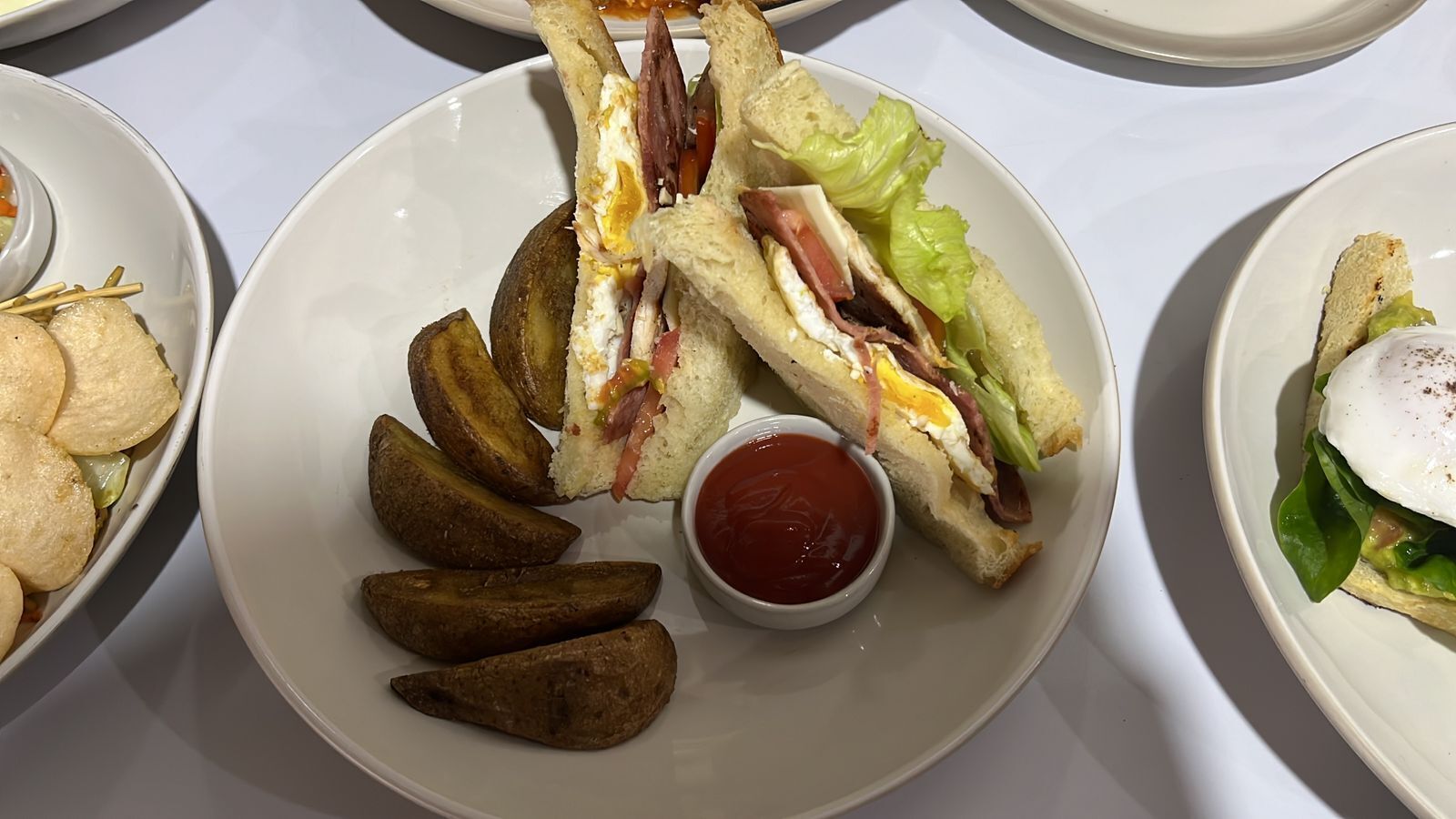 A plate with a sandwich, potato wedges, and a small bowl of ketchup.