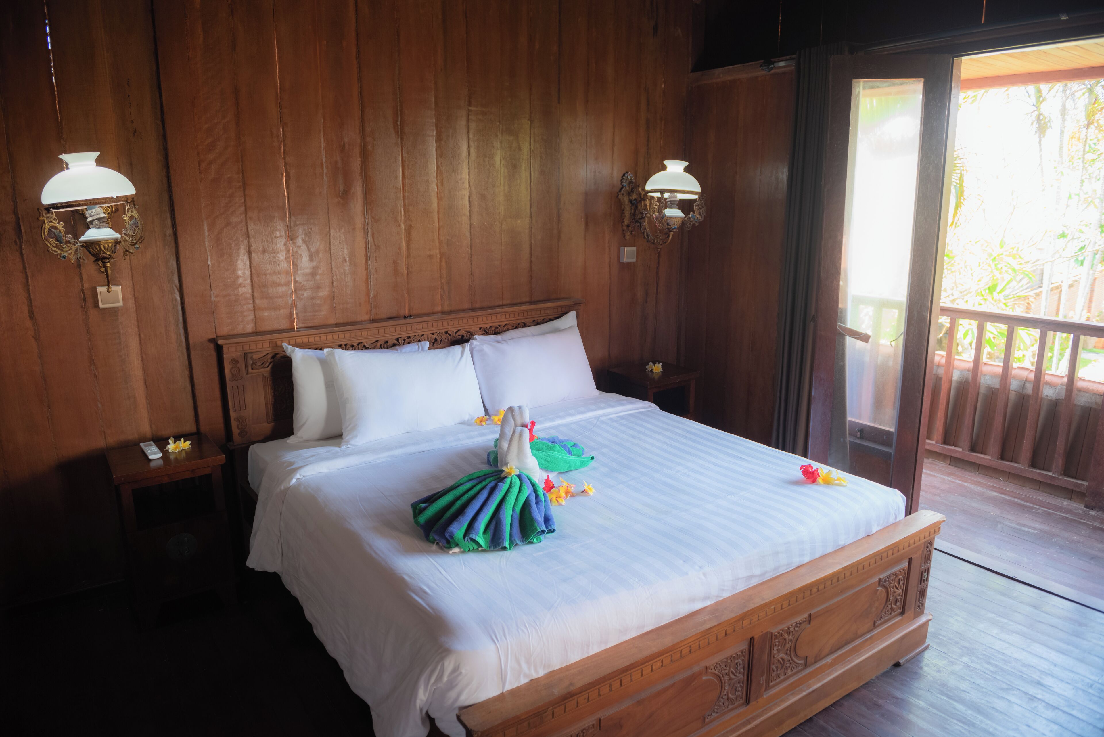 Uma cama de madeira com lençóis brancos, uma toalha com flores e duas luminárias de parede.