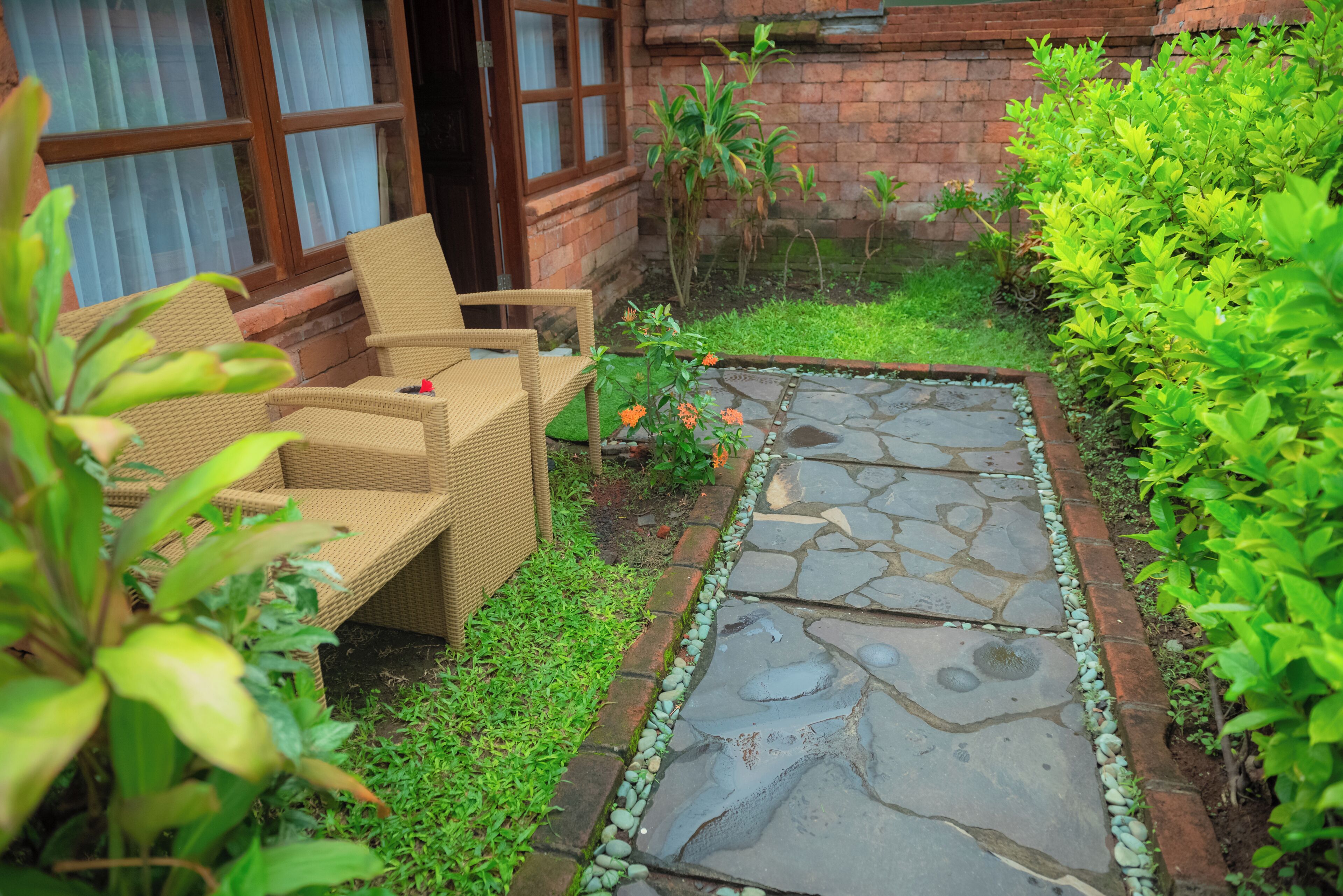 Un sendero en un jardín con pavimento de piedra, una silla de mimbre y una pared de ladrillo.