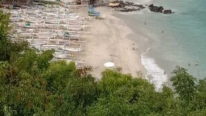 A beach with a forested hill, clear turquoise waters, and a row of beach huts. - The Ariras Resort (Karangasem)