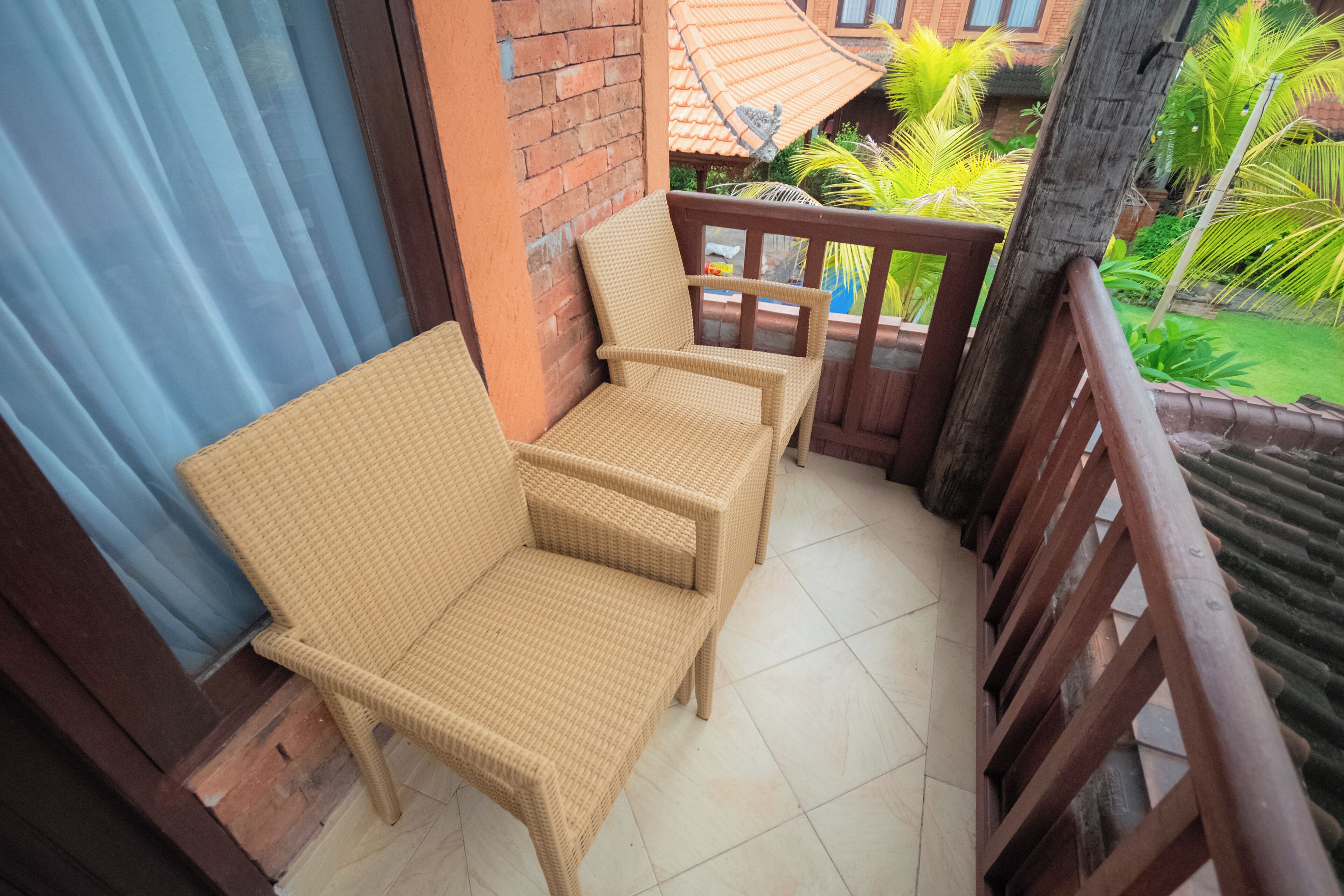 A balcony with wicker furniture, a tiled floor, and a view of a garden with palm trees.
