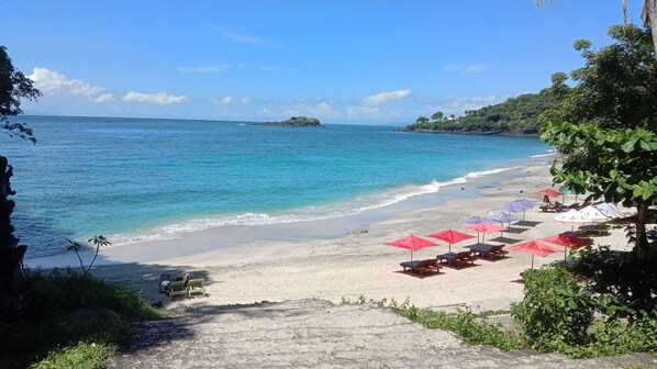 A beach with clear turquoise water, a sandy shore, and several red umbrellas. - The Ariras Resort (Karangasem)