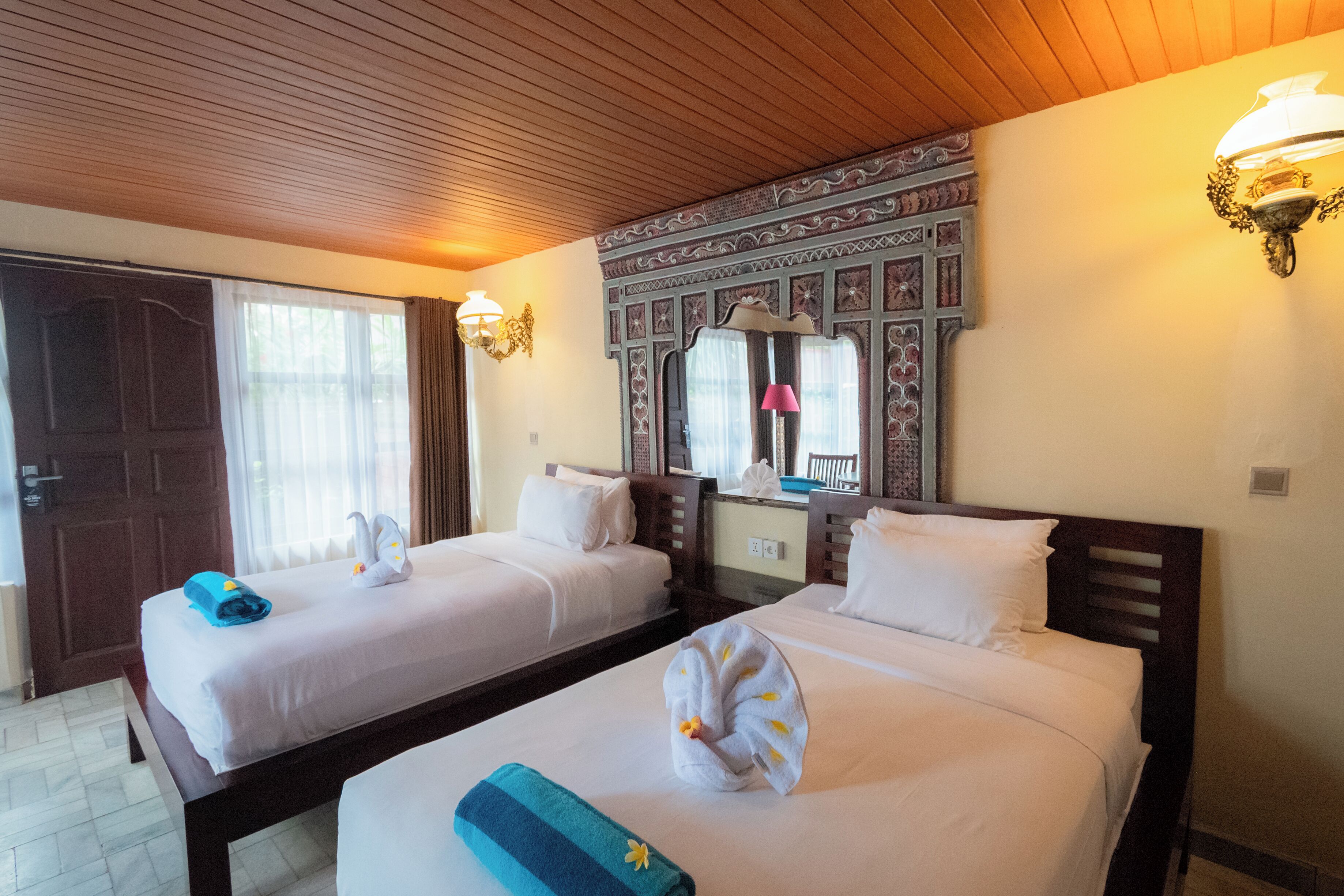 A hotel room with two beds, a wooden ceiling, and a decorative wall panel.