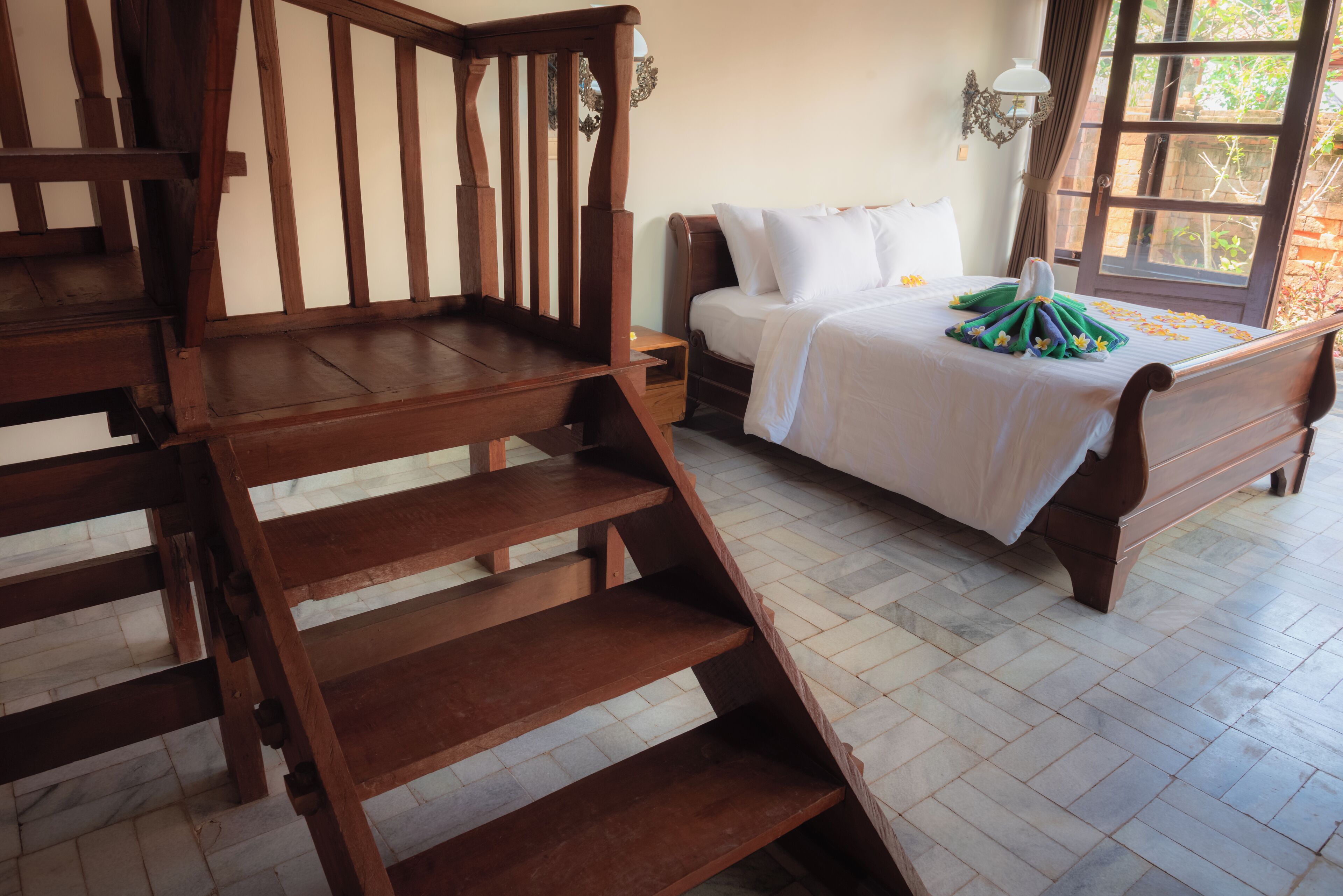 Un dormitorio con escalera de madera, cama con ropa blanca y ventana con vista a follaje.