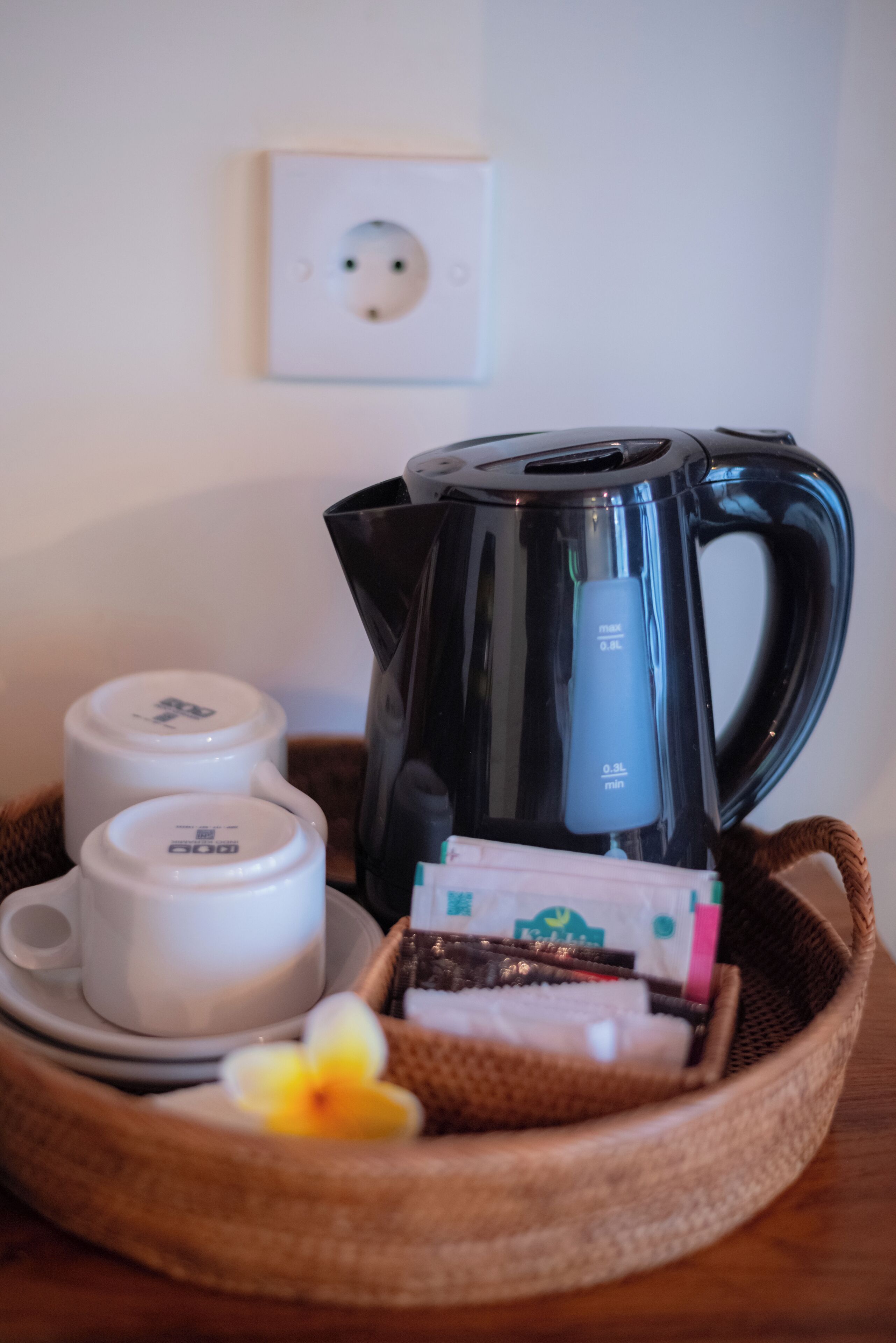 Una cafetera, dos tazas y una cesta con cápsulas de café y una flor sobre una mesa.