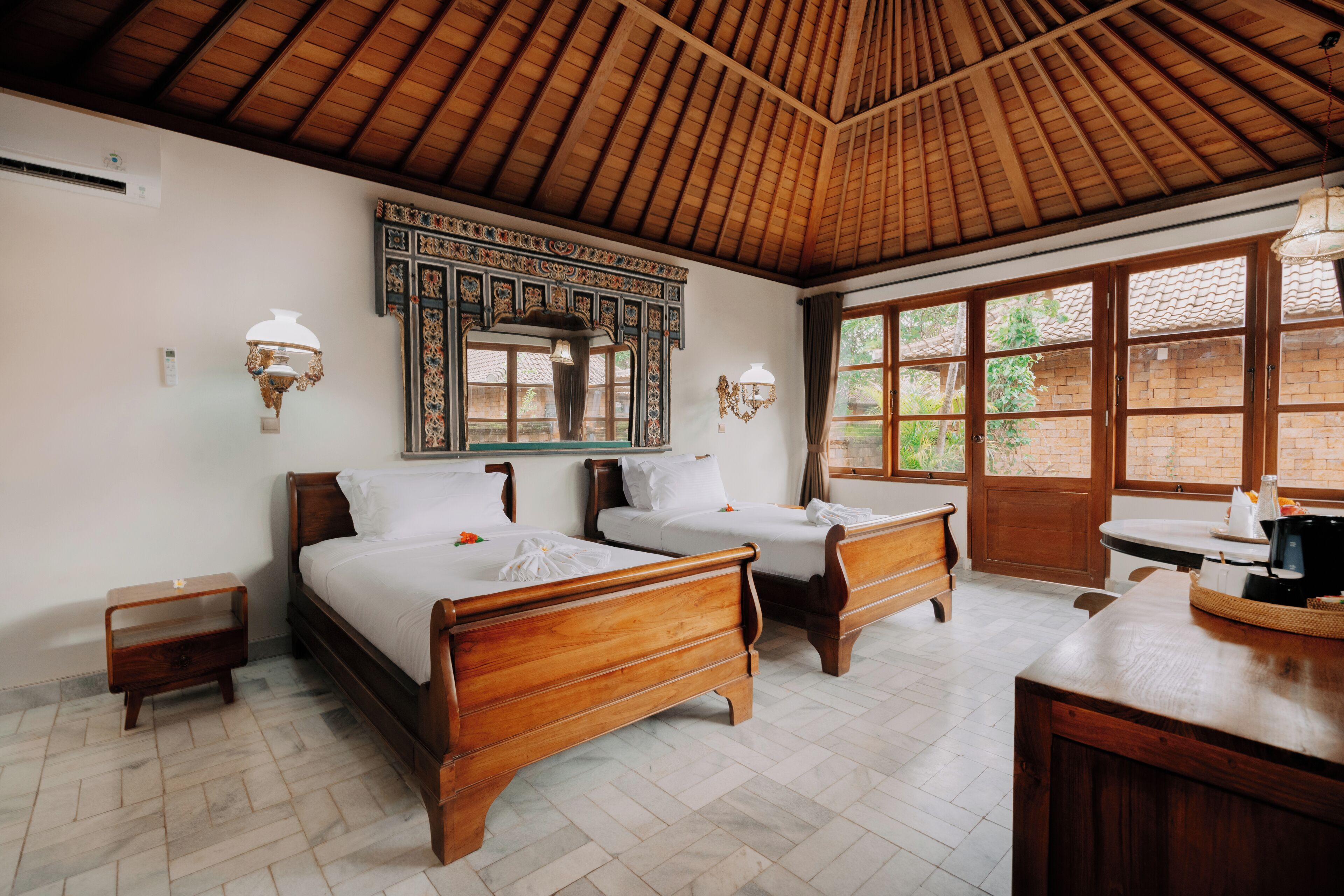 Habitación de hotel con dos camas de madera, techo de madera, un ventanal grande y una pequeña cocina.
