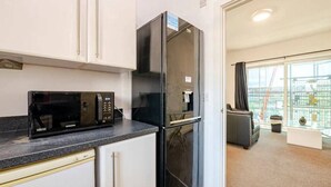 A compact kitchen with a black microwave and refrigerator, white cabinets, and a view of the city through large windows. - 2Bed Apt - City Centre with Balcony - Sleeps 6 (Southampton)