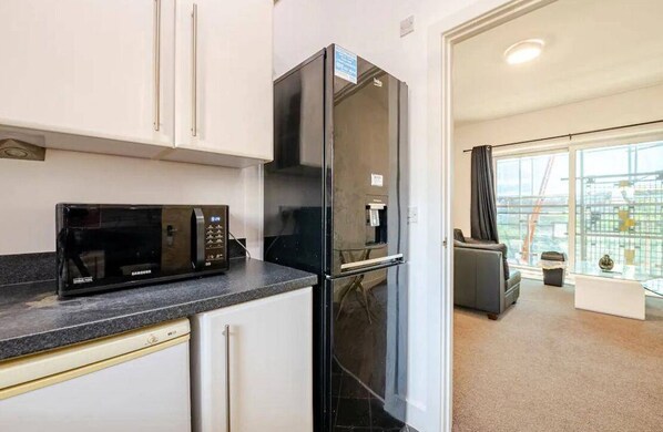 Compact kitchen with modern appliances and adjacent living area featuring a sofa and glass coffee table.