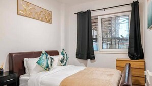 A bedroom with a bed, a nightstand, a dresser, a window with curtains, and a wall-mounted artwork. - 2Bed Apt - City Centre with Balcony - Sleeps 6 (Southampton)
