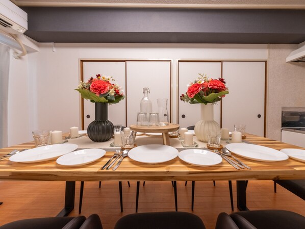 A dining table set for six with white plates, silverware, and two vases with red flowers. -  Mobius Yasaka Namba Family Suite (Osaka)