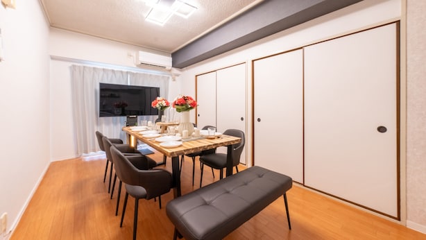 A dining area with a wooden table set for four, black chairs, and a bench. There is a vase with flowers on the table. -  Mobius Yasaka Namba Family Suite (Osaka)