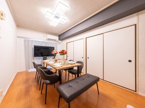A dining area with a wooden table set for four, black chairs, and a bench. There is a vase with flowers on the table. -  Mobius Yasaka Namba Family Suite (Osaka)