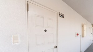 Una porta bianca con un cartello sopra, un interruttore della luce e un allarme antincendio sul muro.