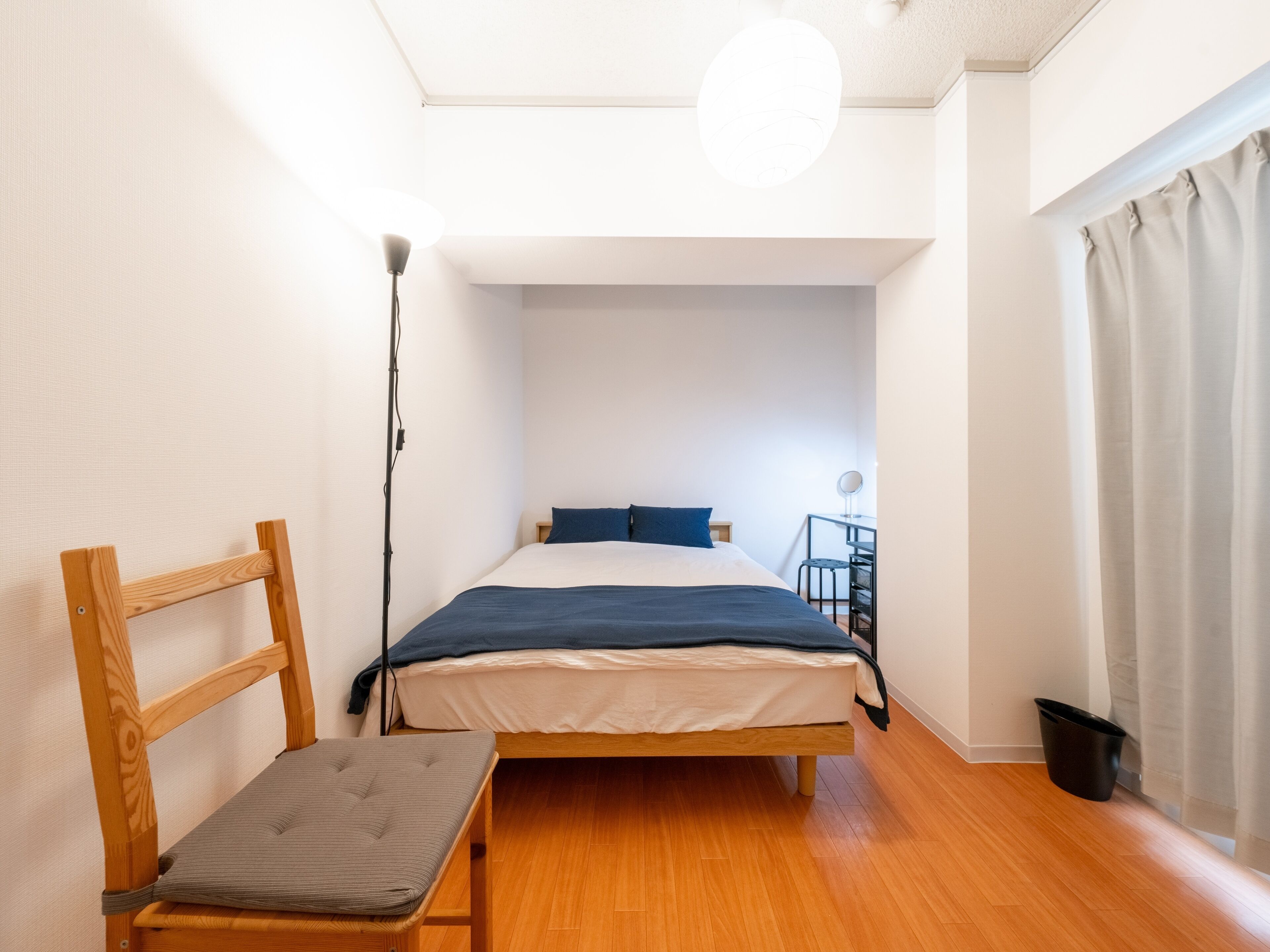 Un dormitorio pequeño y bien iluminado, con una cama de madera, un escritorio con silla y una mesita de noche.