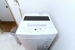 A white washing machine with a digital display and control panel, placed against a white wall. -  Mobius Yasaka Namba Family Suite (Osaka)