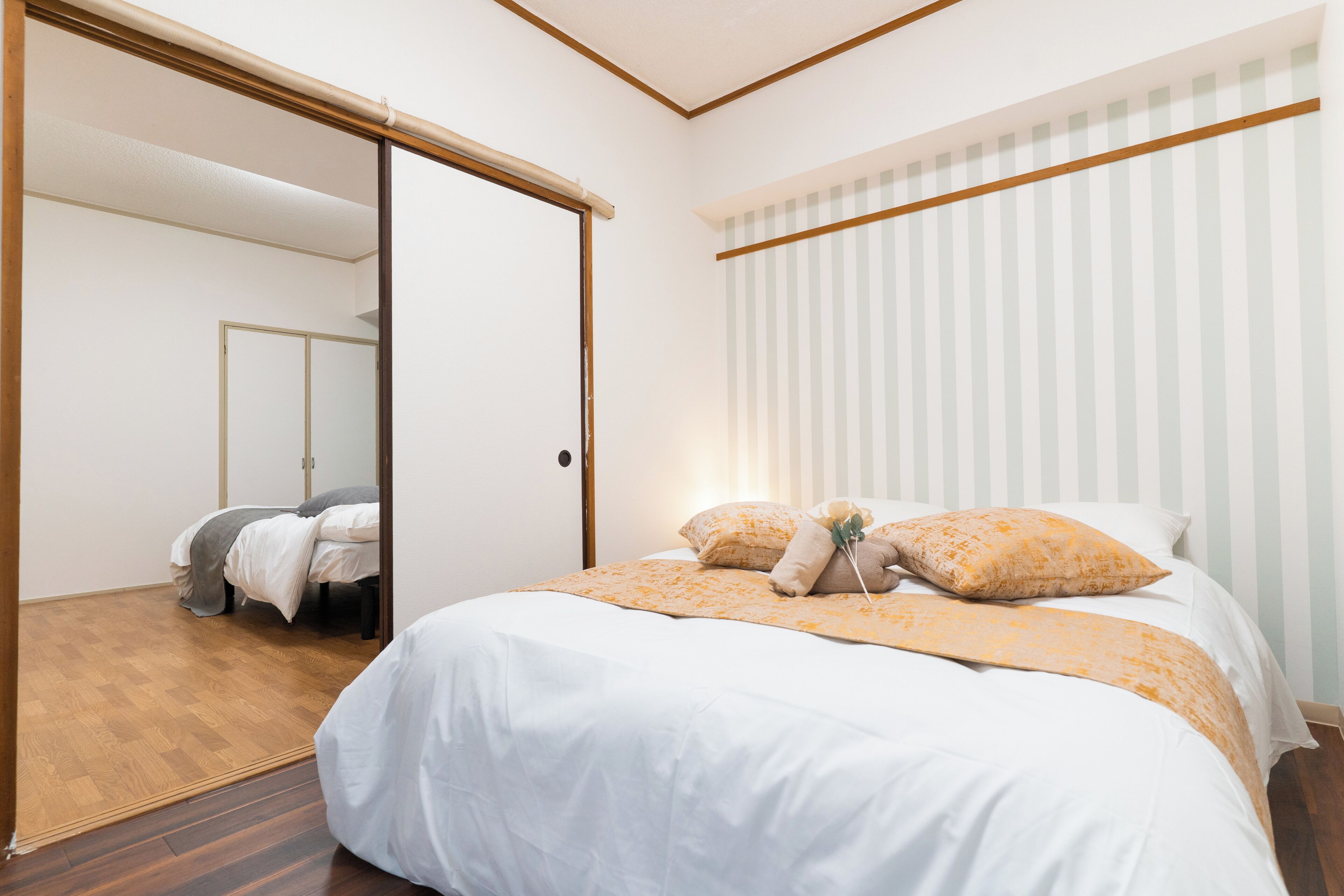 A hotel room with a bed, a mirror, a window with blinds, and a wooden floor.